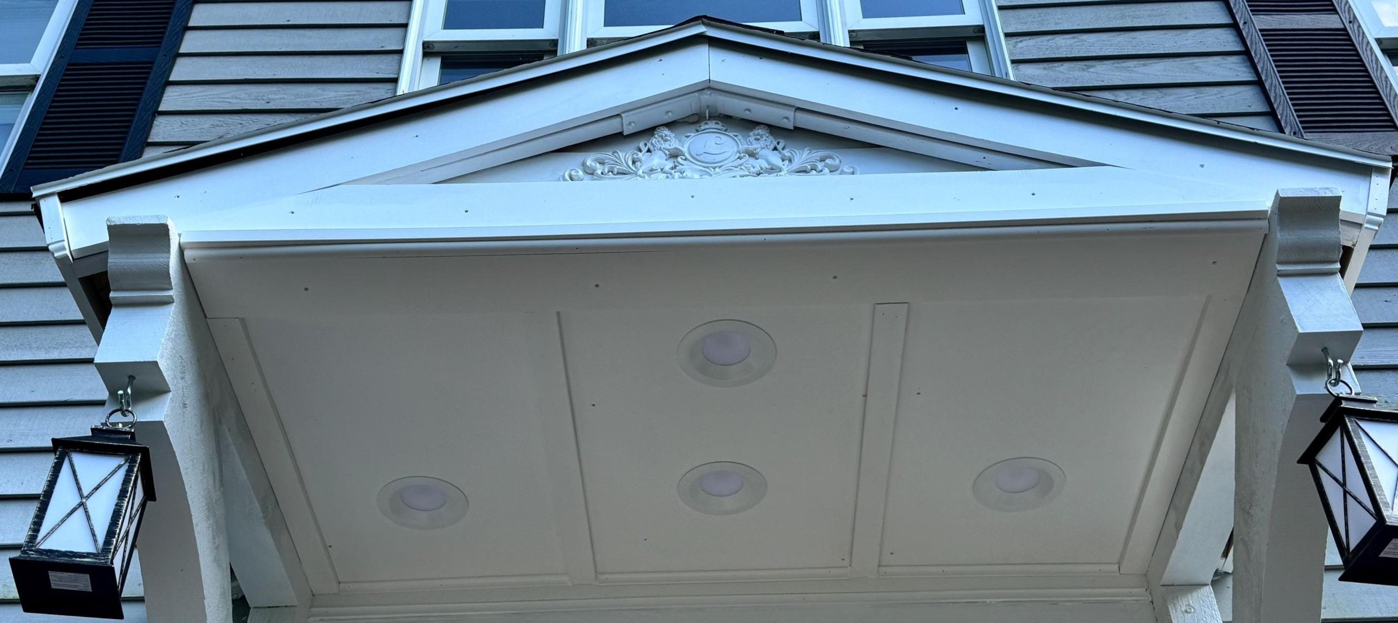 An elegant white patio cover with gable roof, with recessed lights in ceiling and decorated with two hanging lamps.