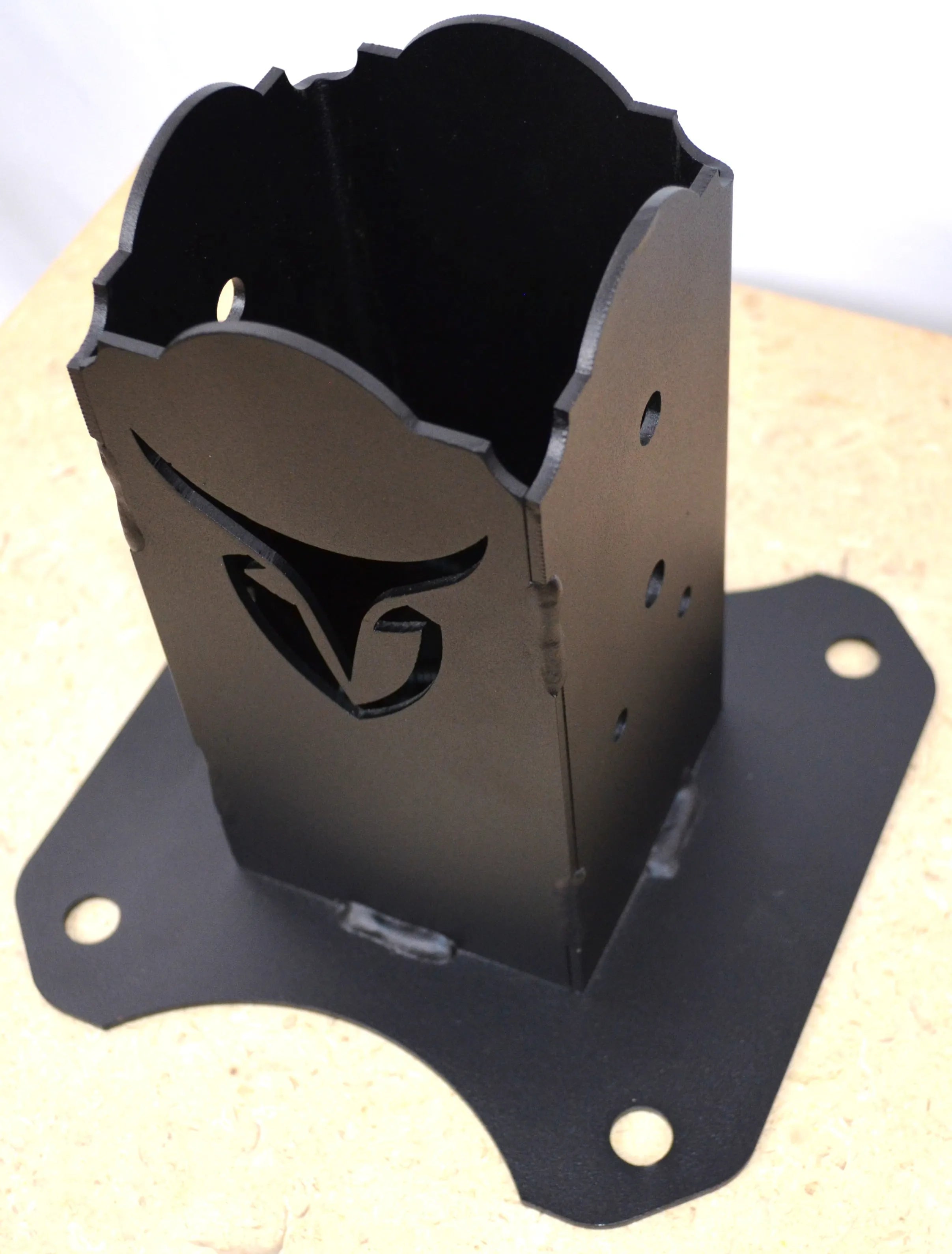 A black metal mounting holder stands on a flat surface, showcasing its unique design and multiple mounting holes, making it versatile for different uses.