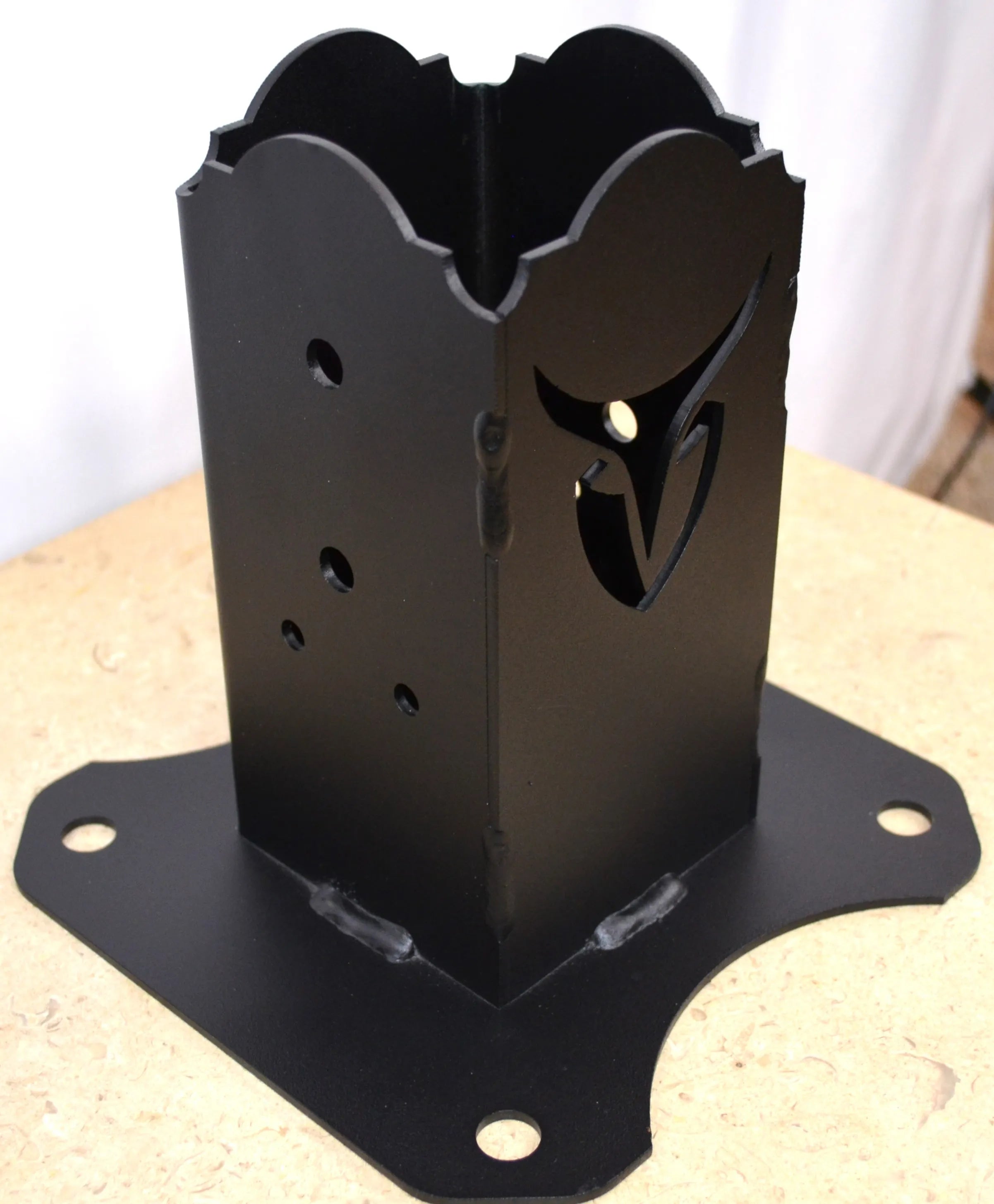 A black metal floor anchor stands on a flat surface, showcasing its unique design and multiple mounting holes, making it versatile for different uses.