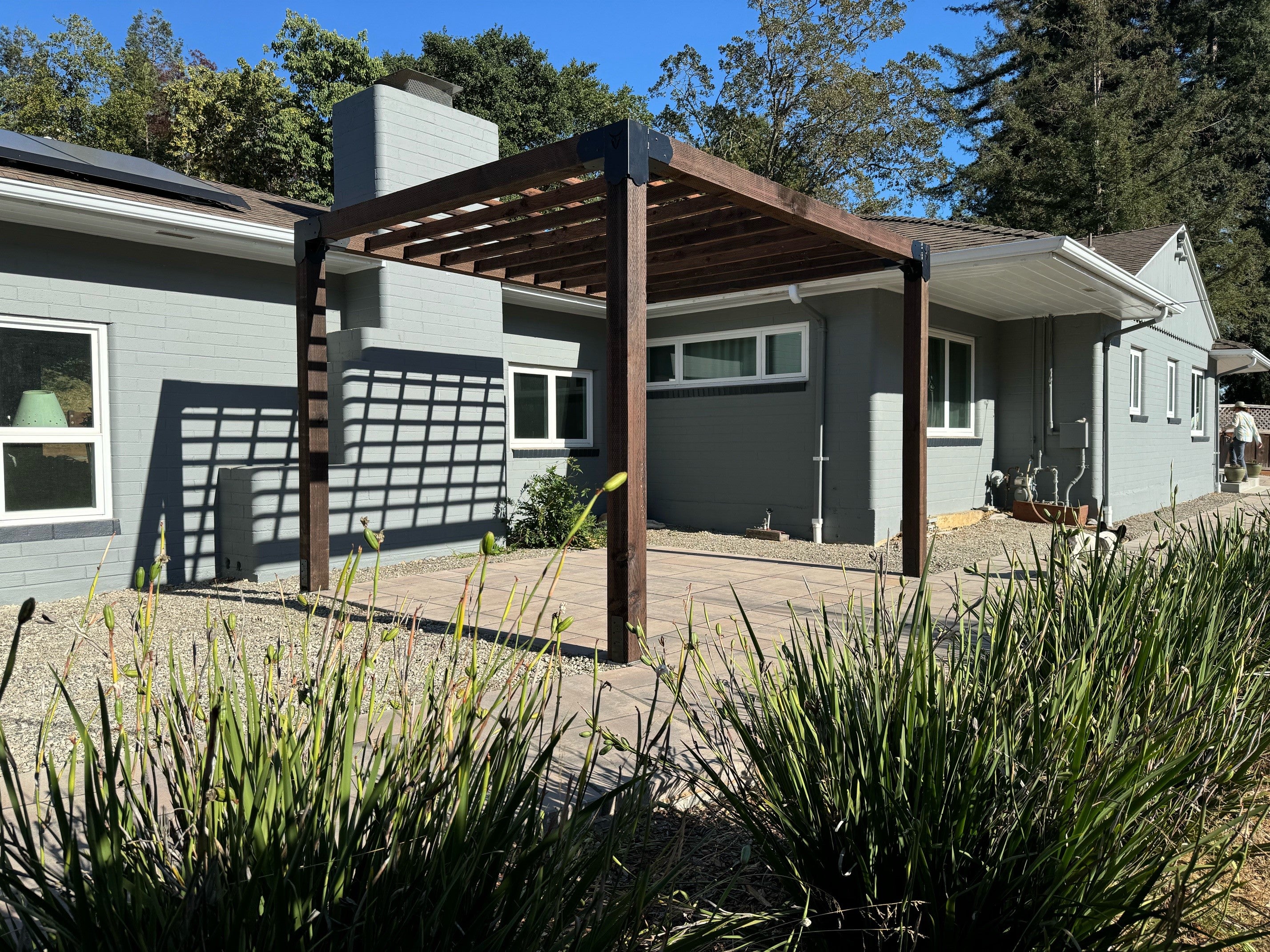 Rectangle pergola with roof slats next to a house on a sunny afternoon