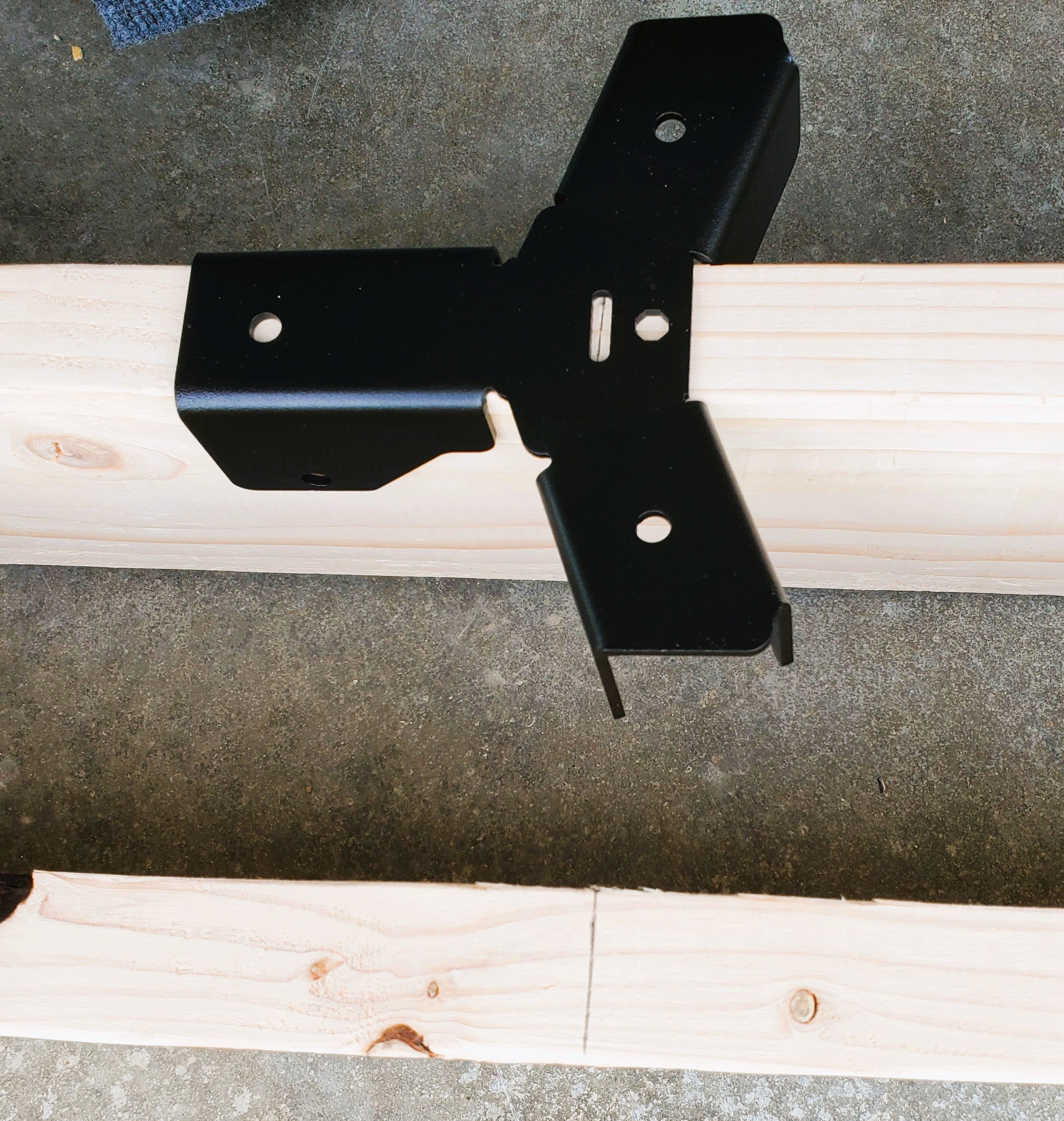 An octagon cross-tie bracket is attached to a wooden structure, showcasing a pencil mark viewing window that aids in precise alignment during installation.