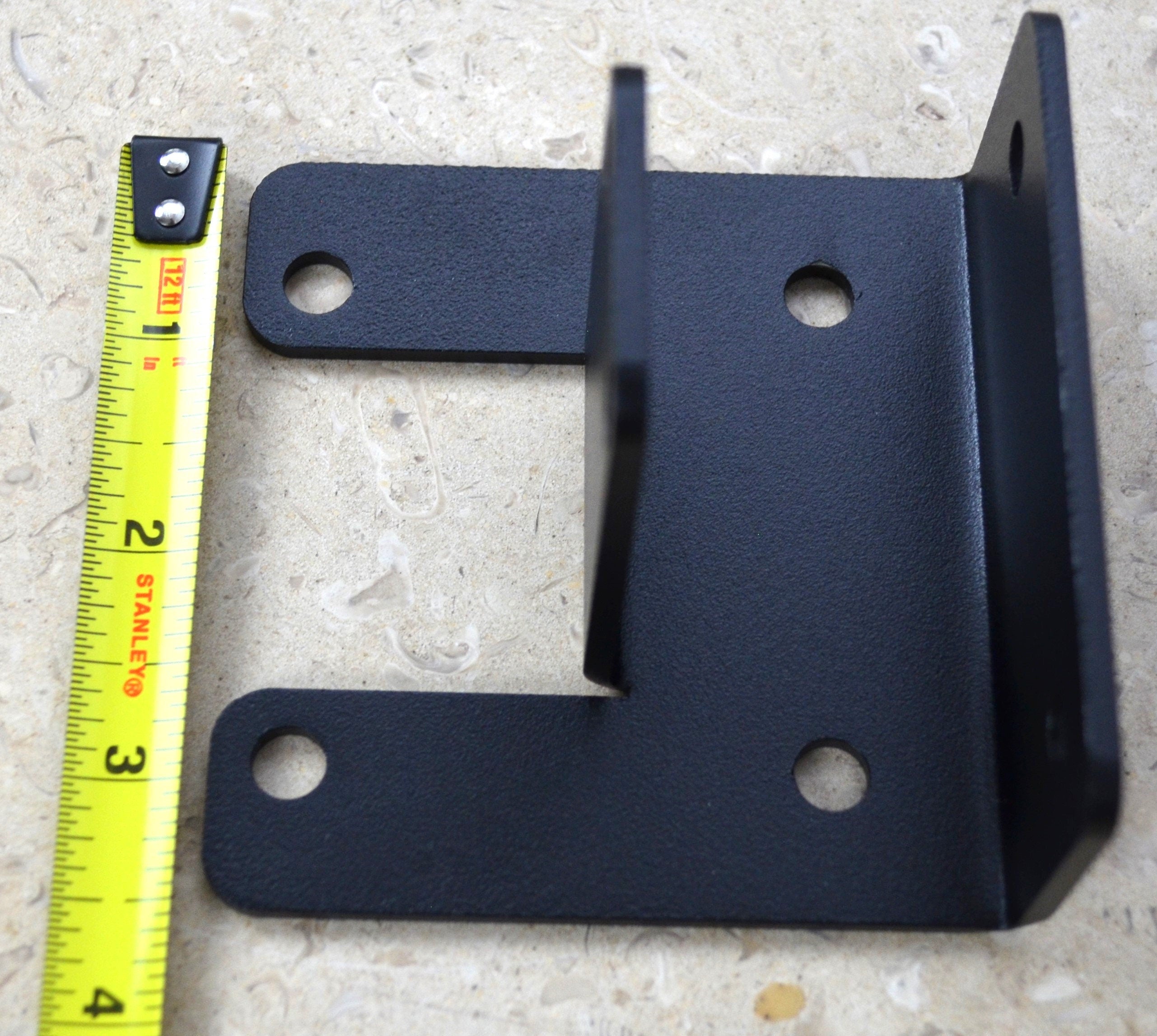 A black metal corner bracket is displayed, designed to provide support and stability in various construction applications. Ideal for DIY projects and repairs.