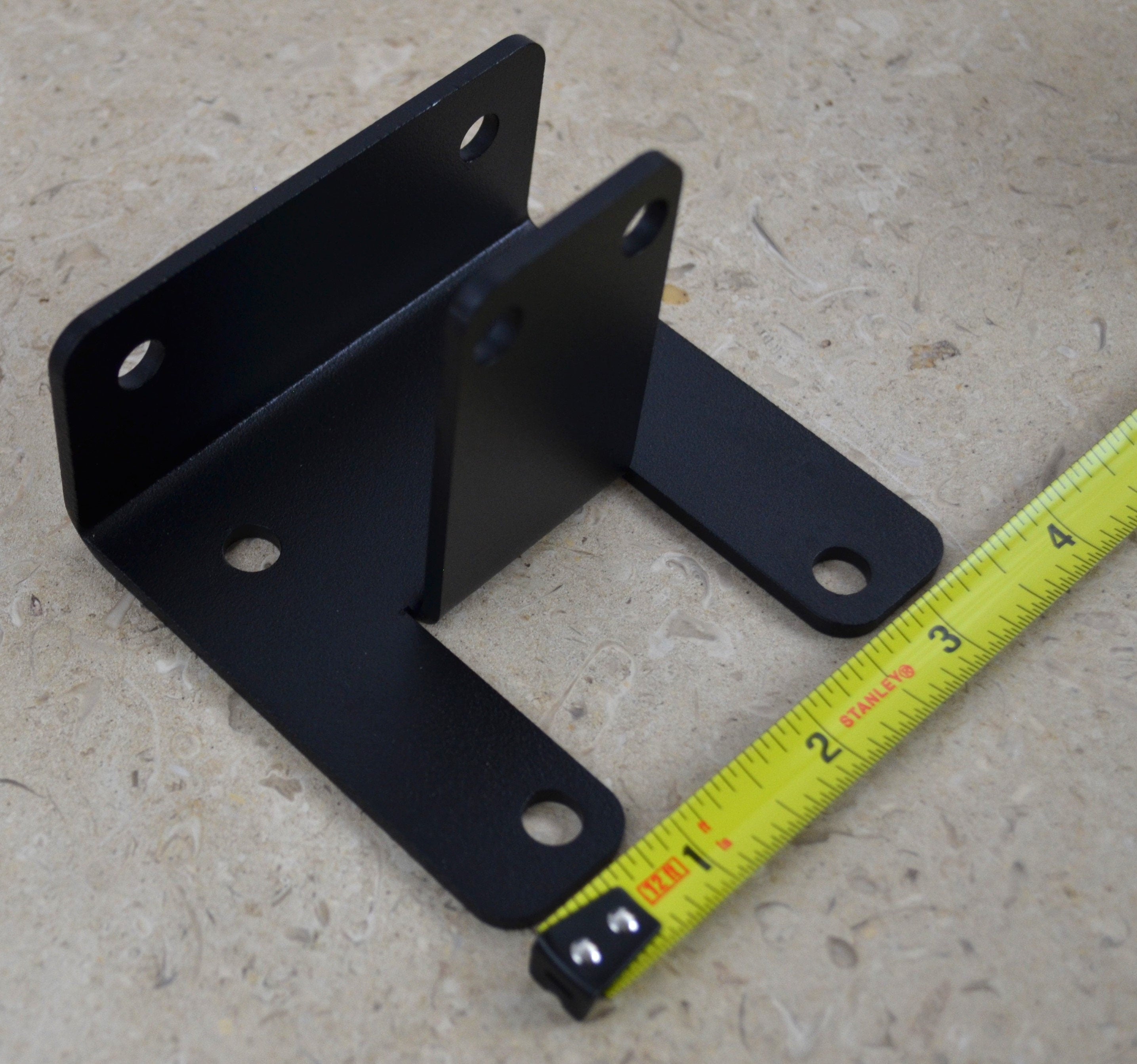 A black metal corner bracket is displayed, designed to provide support and stability in various construction applications. Ideal for DIY projects and repairs.