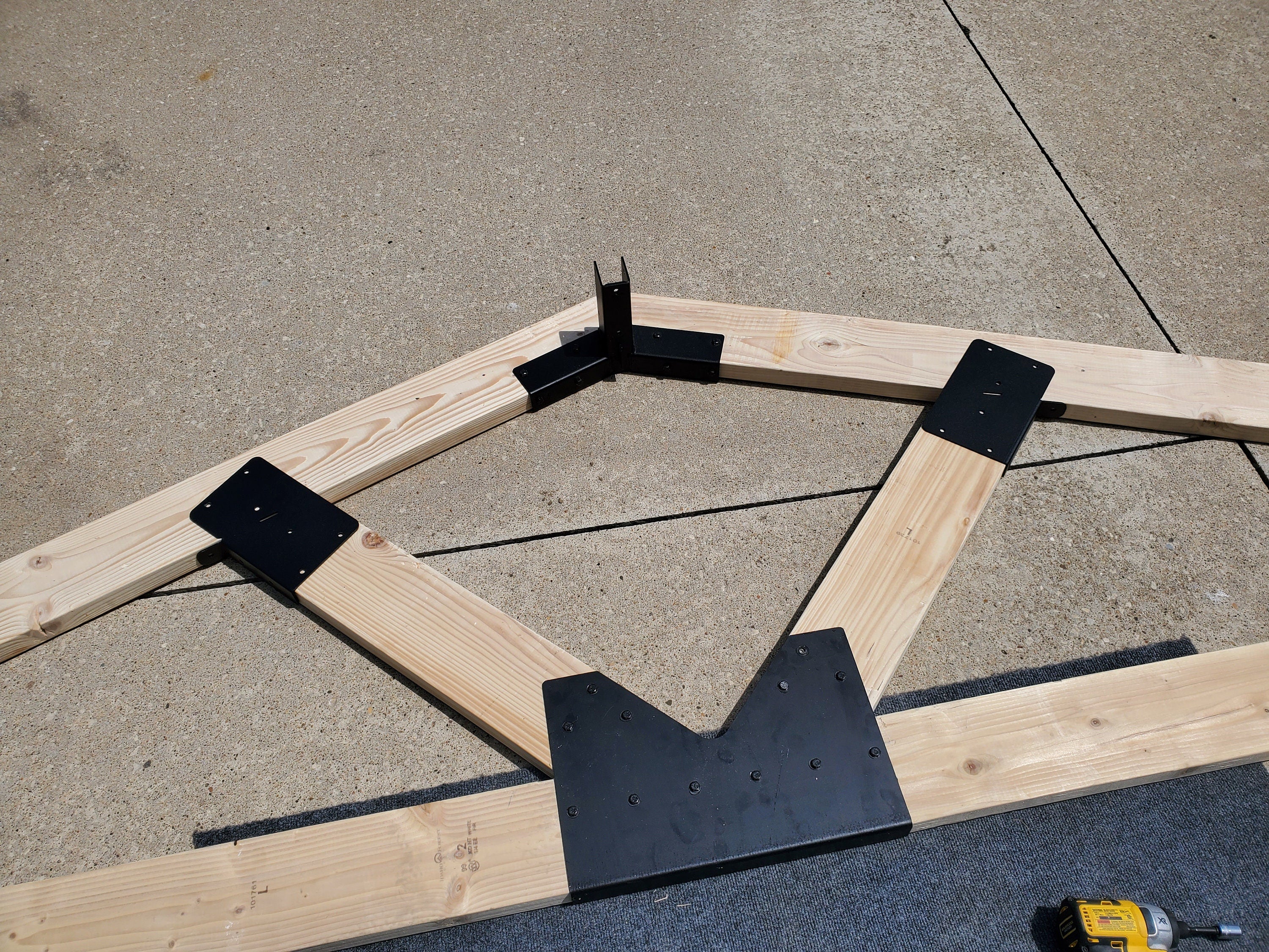 A wooden truss frame is being assembled using metal brackets. The structure showcases detailed craftsmanship with carefully arranged lumber pieces and secure fittings.