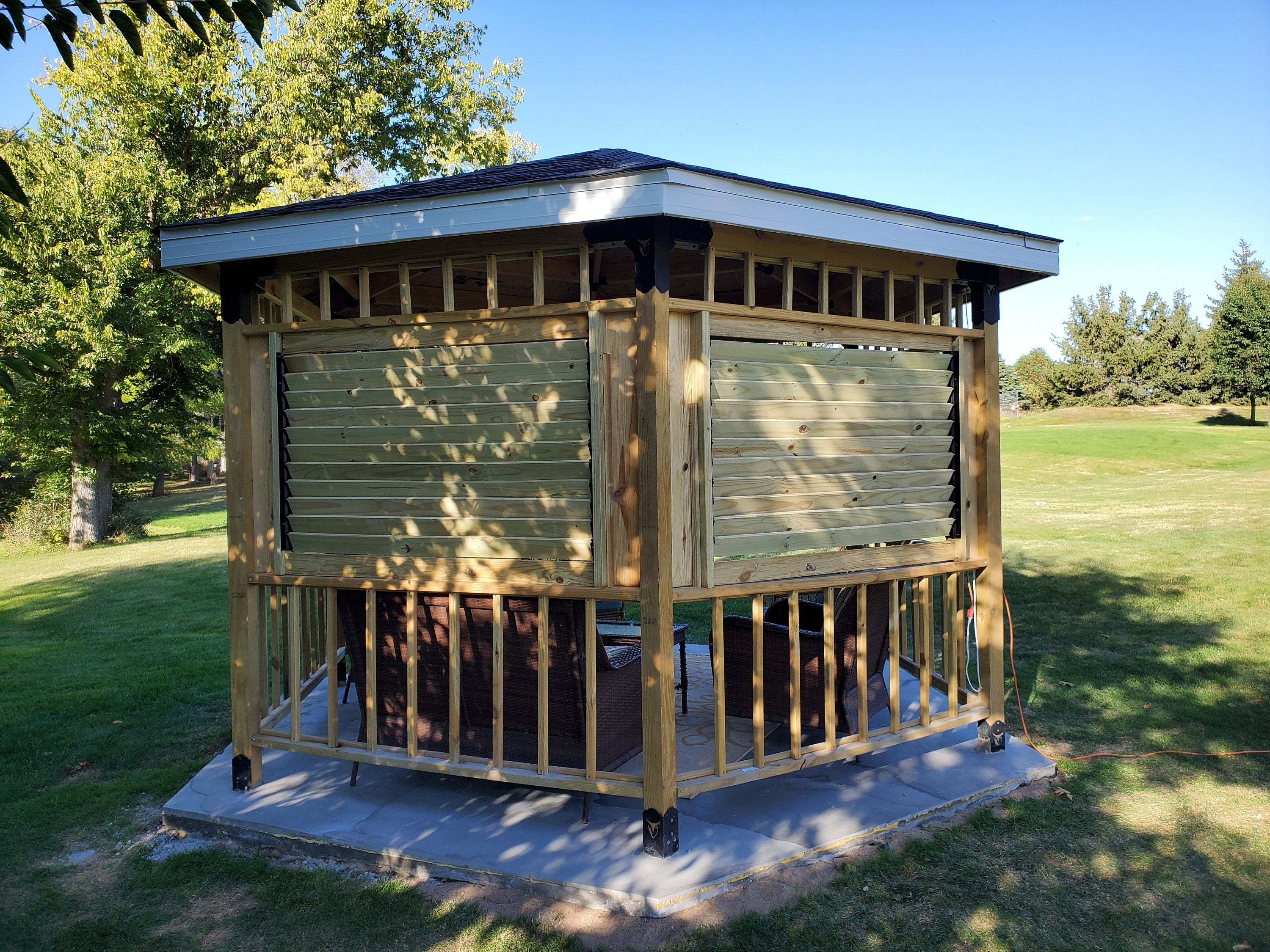 The cozy gazebo features comfortable seating with cushions and a relaxed atmosphere, ideal for enjoying sunny days in a lush garden.