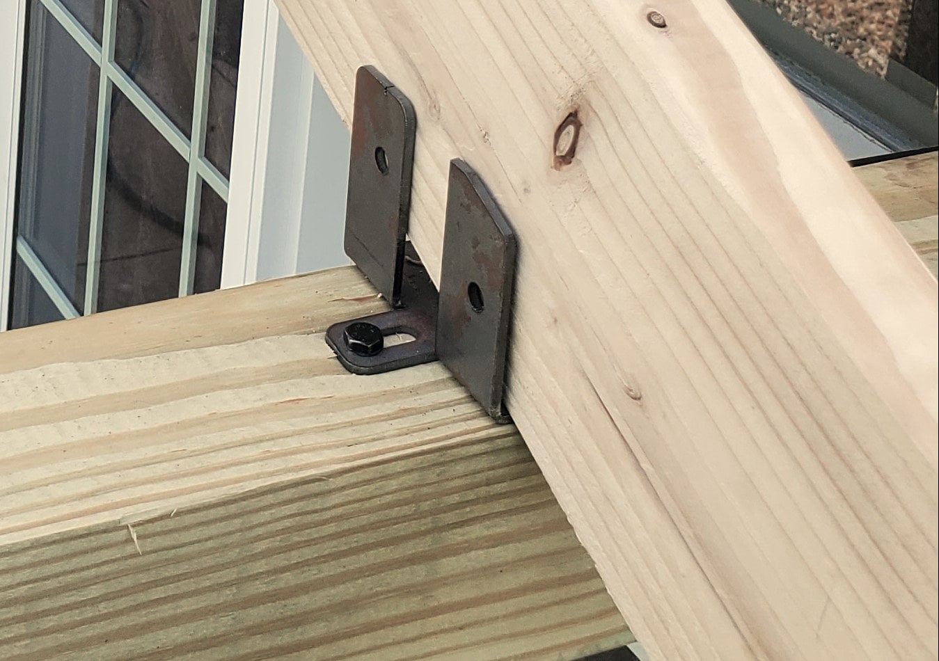 Metal brackets secure two timber beams together at a residential construction site, showcasing details of structural support. The work highlights craftsmanship and precision.