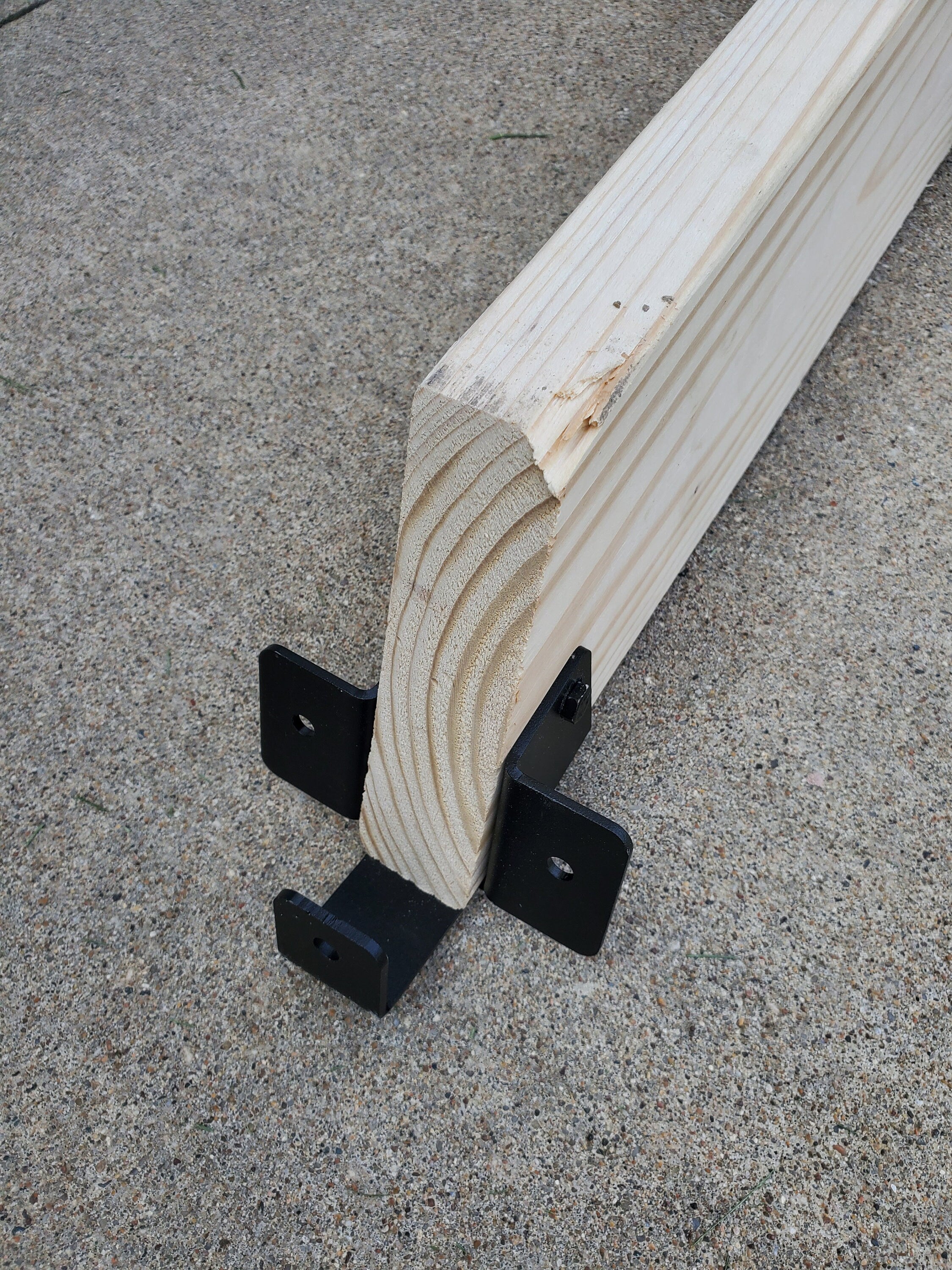 Two metallic brackets are securely fastened to a wooden beam, providing sturdy support in a construction workshop environment, demonstrating functional design.