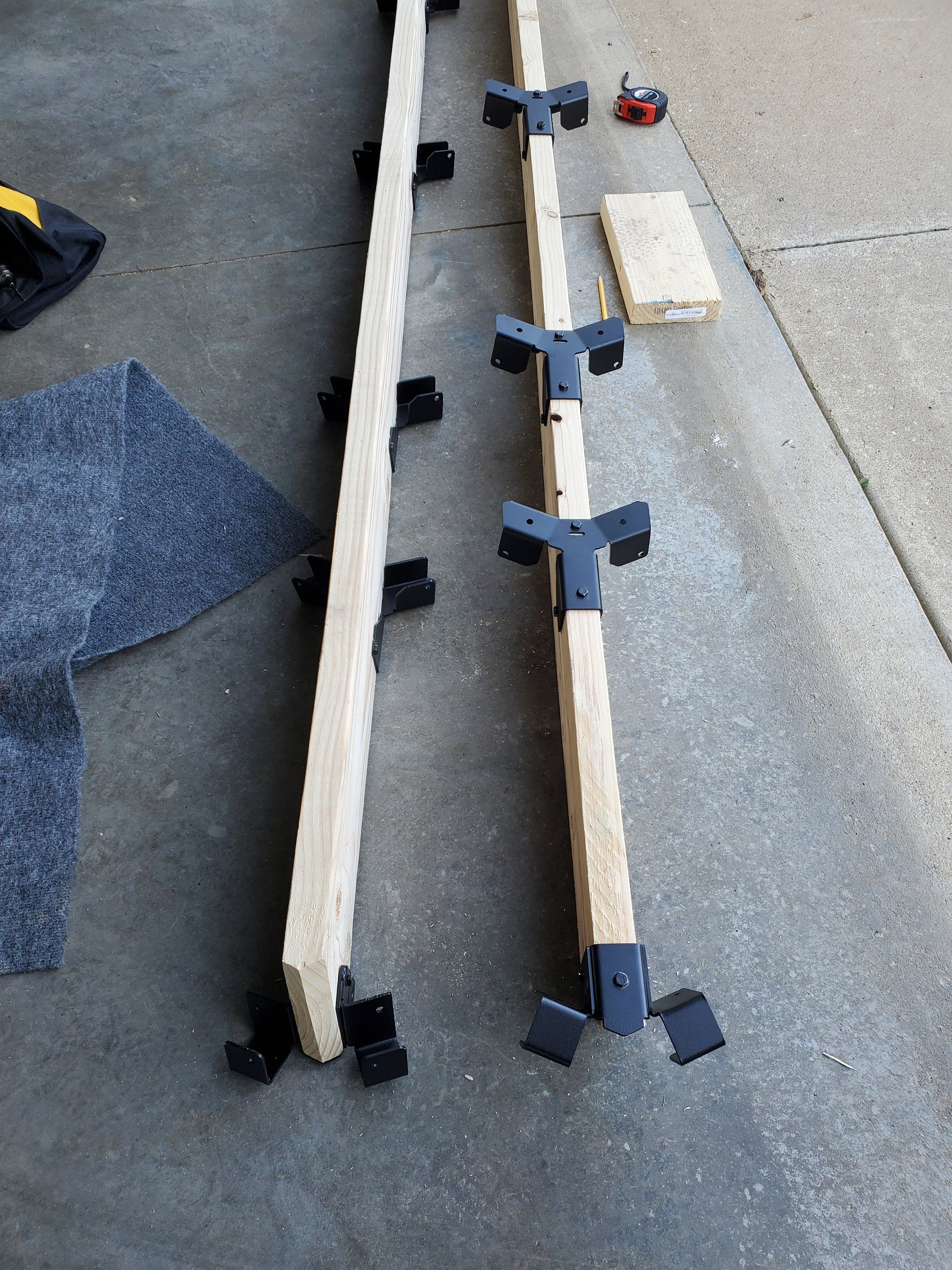 Two wooden planks secured with metal brackets rest on a concrete floor in a workshop setting, indicating preparations for a construction project.