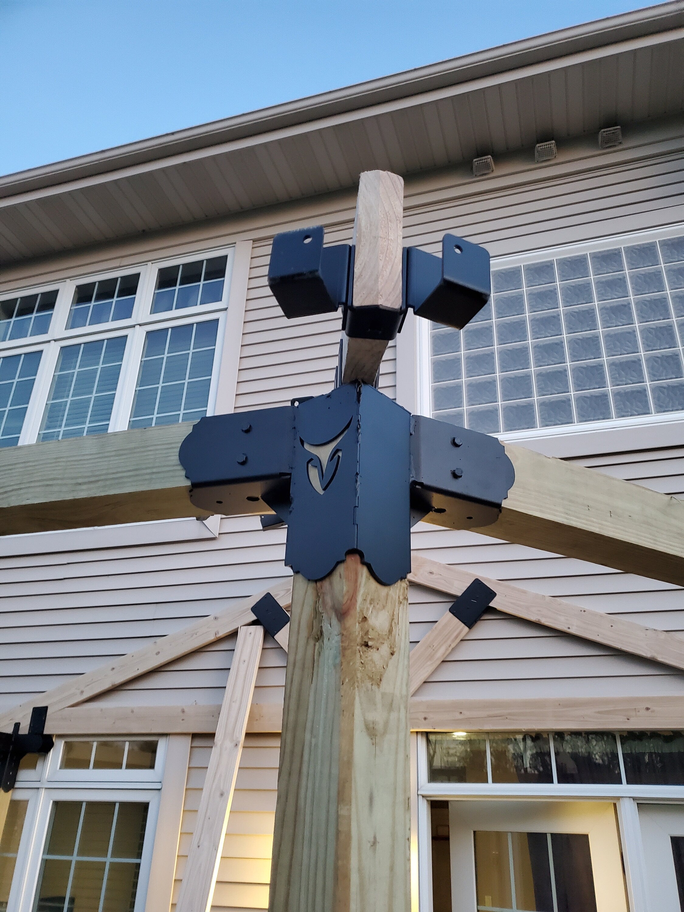 A wooden framework is being assembled, showcasing metal connectors designed to enhance stability. The project is situated in a residential area under clear skies.