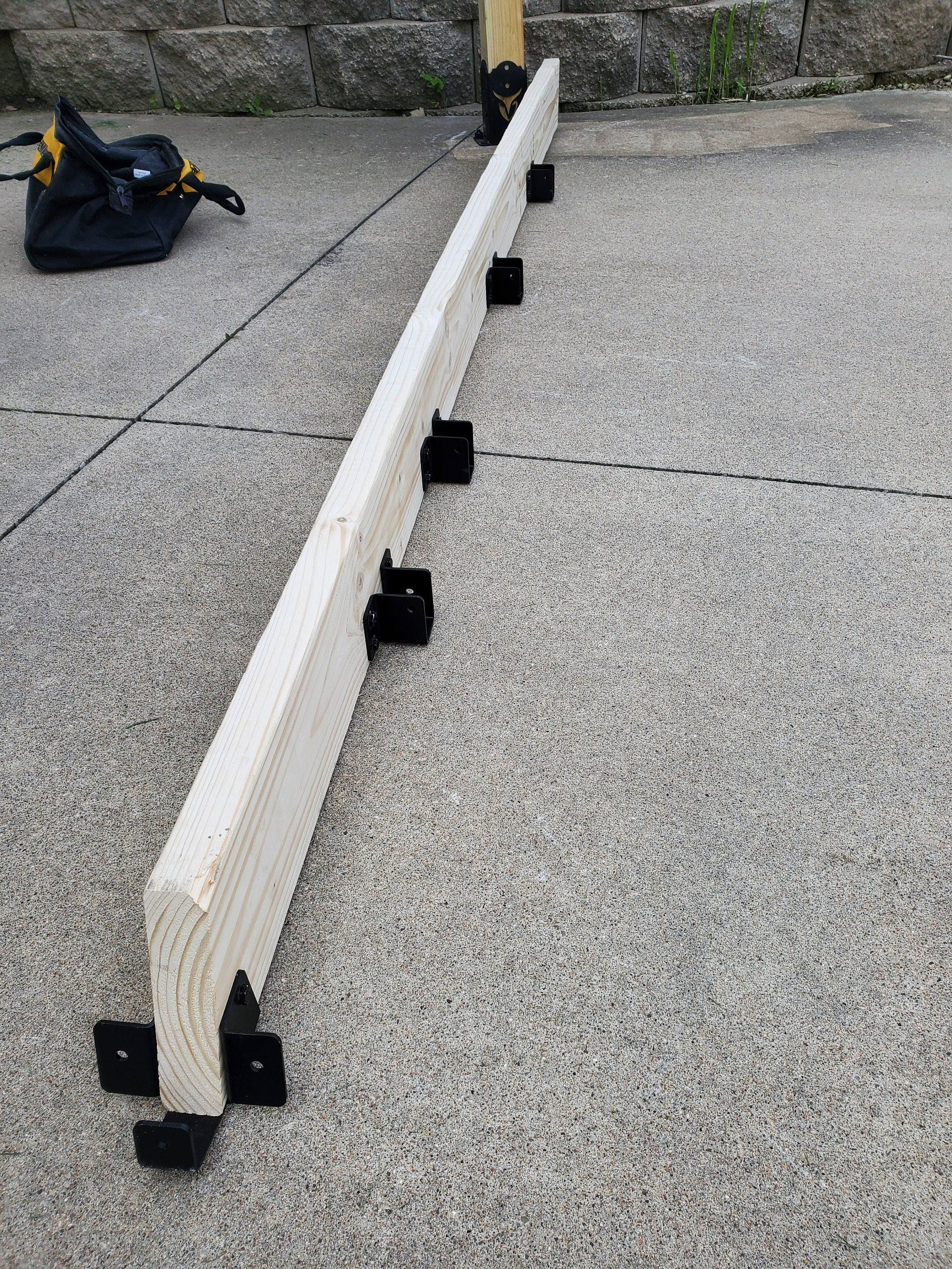 Two metallic brackets are securely fastened to a wooden beam, providing sturdy support in a construction workshop environment, demonstrating functional design.